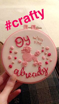 a person holding up a pink and white embroidered badge with the words crafty on it