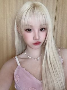 a doll with long blonde hair wearing a pink dress and pearls on her necklace, posing for the camera