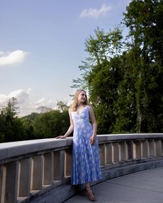a woman in a blue and white dress standing on a bridge with trees in the background