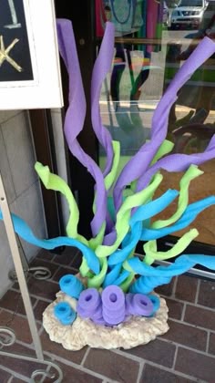 a vase filled with purple and green fake seaweed on top of a brick sidewalk