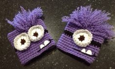 two purple knitted hats with eyes on them sitting on top of a black counter