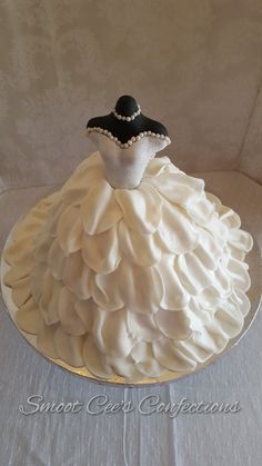 a wedding dress cake sitting on top of a white tablecloth covered table with a black and white hat
