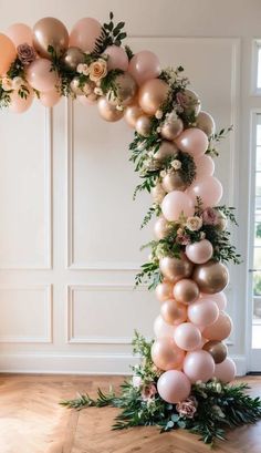 the balloon arch is decorated with pink and gold balloons, greenery, and flowers