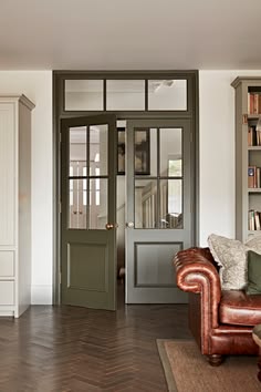 a brown leather couch sitting in front of a green door on top of a hard wood floor