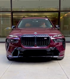the front end of a red bmw suv parked in front of a glass building with large windows