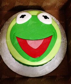 a cake decorated to look like kermie the frog with big eyes and mouth