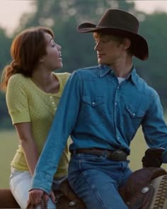a man riding on the back of a brown horse next to a woman wearing a cowboy hat