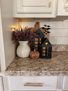 a white vase filled with purple flowers next to a halloween decoration on top of a kitchen counter