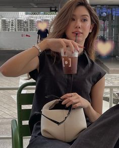 a woman sitting in a chair holding a drink and looking at the camera with her hand on her hip