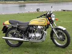 a yellow and black motorcycle parked on top of a lush green field next to a lake