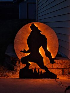 the silhouette of a man with a hat on is lit up in front of a house