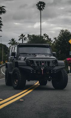 a black jeep driving down the road with palm trees in the background