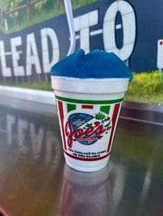 a cup with blue stuff in it sitting on top of a metal table next to a sign