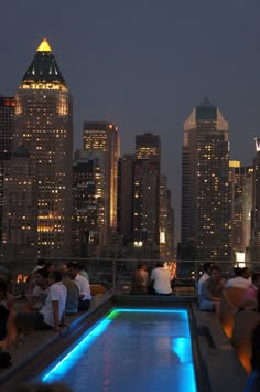 people are sitting on the roof of a building at night with city lights in the background