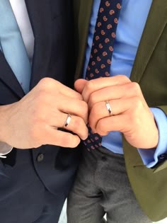 two people in suits and ties holding hands with their wedding rings on top of each other
