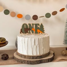 a white cake sitting on top of a table next to a wooden sign that says one