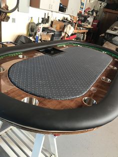 a wooden table with black leather seat pad and metal legs in a garage area next to other workbench equipment