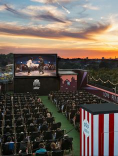an outdoor movie theater at sunset with people sitting in chairs watching the movies on the screen