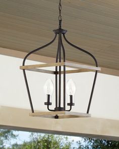 a light fixture hanging from the ceiling in front of a porch with trees and bushes
