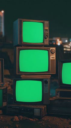 four old televisions with green screen sitting on the ground in front of each other