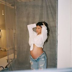 a pregnant woman standing in front of a mirror with her hands on her head and arms behind her head