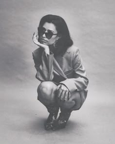 a black and white photo of a woman in sunglasses sitting on the ground with her hand near her face