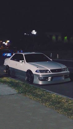 a white car parked on the side of a road at night with police lights in the background