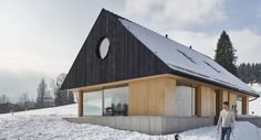 a man standing in the snow next to a small house on top of a hill