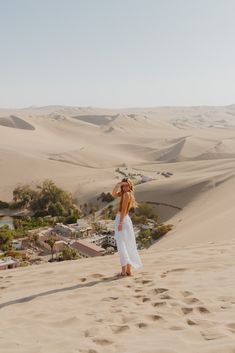 a woman standing on top of a sandy hill next to a desert town and trees