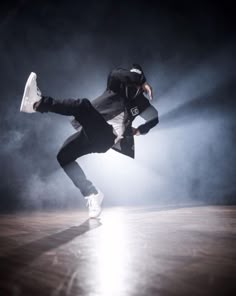 a man in black jacket and white sneakers doing a dance move on a wooden floor