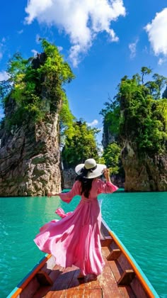 a woman in a pink dress and hat riding on a boat through the blue water