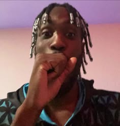 a man with dreadlocks is holding his hand up to his mouth and looking at the camera