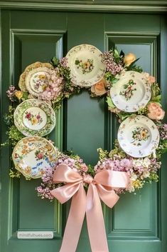a wreath with flowers and plates hanging on the front door, decorated with pink ribbon
