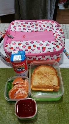 a lunch box with toast, fruit and jam on the table next to an orange juice