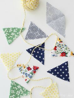 several pieces of fabric hanging from twine on a white surface with balls of yarn in the background