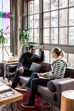 a man and woman sitting on a couch in front of a window with a laptop