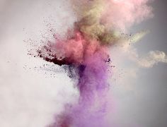 colorful powder is thrown into the air in front of a gray sky with white clouds