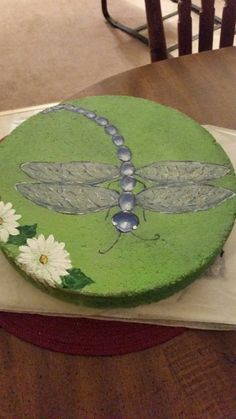 a green cake with a dragonfly on it sitting on a table next to flowers