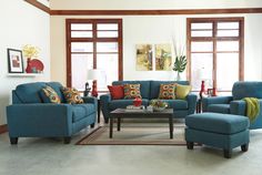 a living room with blue couches and colorful pillows on the rugs in front of two windows