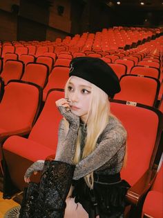 a woman sitting in an empty auditorium with red chairs behind her and looking off to the side