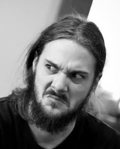 a man with long hair and beard wearing a black shirt is looking at the camera