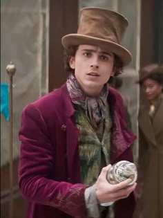 a man in a top hat and coat holding a small object while standing next to another person