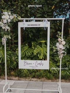 a wedding photo frame with flowers and greenery on the side of a sidewalk in front of trees