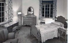 an old black and white photo of a bedroom with a bed, chair, dresser and mirror