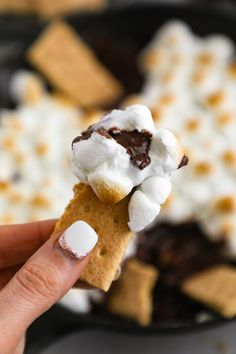 a hand holding a cracker with marshmallows on it and the words, the best s'mores skillet dip