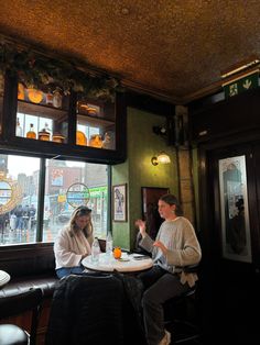 two people sitting at a table with drinks in front of them and looking out the window