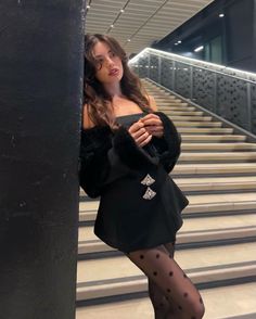 a woman leaning against a pillar in front of some stairs wearing tights and stockings
