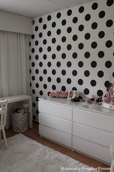 a room with black and white polka dots on the wall next to a dresser in front of a window