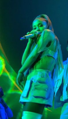 a woman standing on top of a stage holding a microphone in her hand and wearing white pants