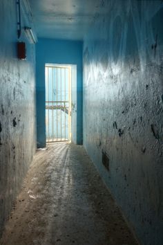 an empty hallway with blue walls and bars on the doors is seen in this image